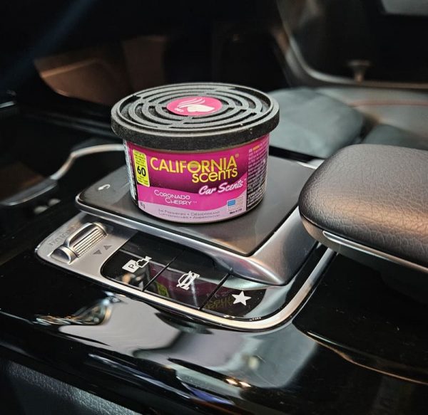 Ambientador CAR SCENTS Coronado Cherry colocado en el portavasos de un coche, liberando su fragancia a cereza.